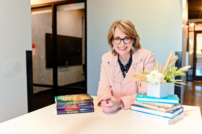 Smiling woman sitting with elbows on desk with stacks of books