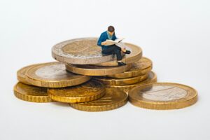 miniature man reading sitting on coins