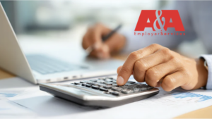 View of person's hands typing on calculator and holding pen while working on laptop